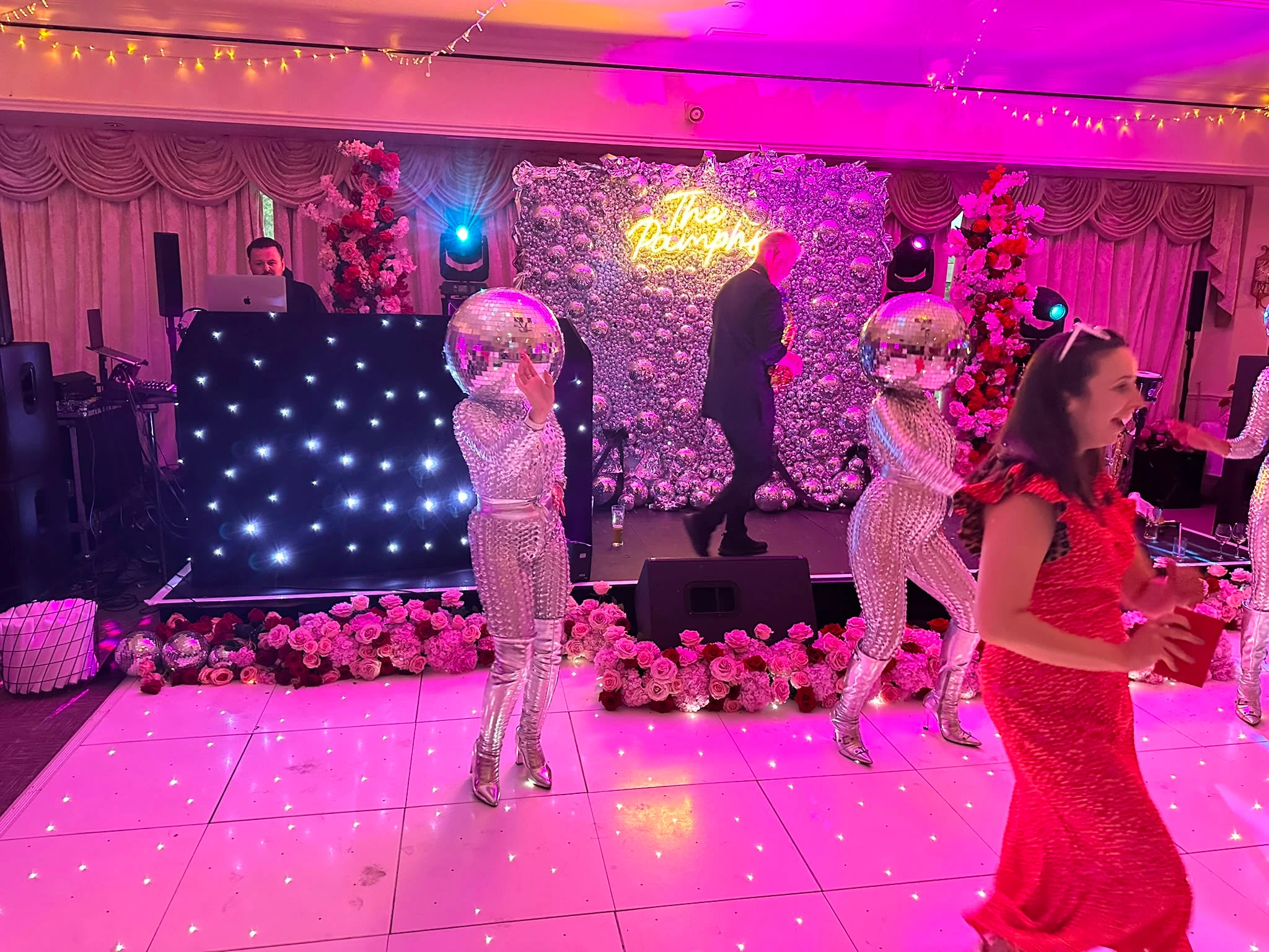 A packed white LED dance floor at a flower-wall party
