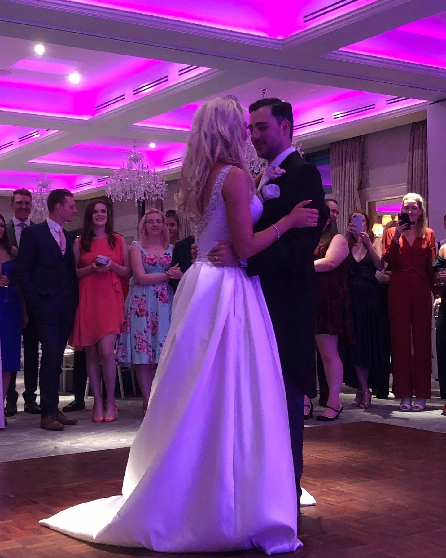 First dance in a ballroom under a pink-lit ceiling