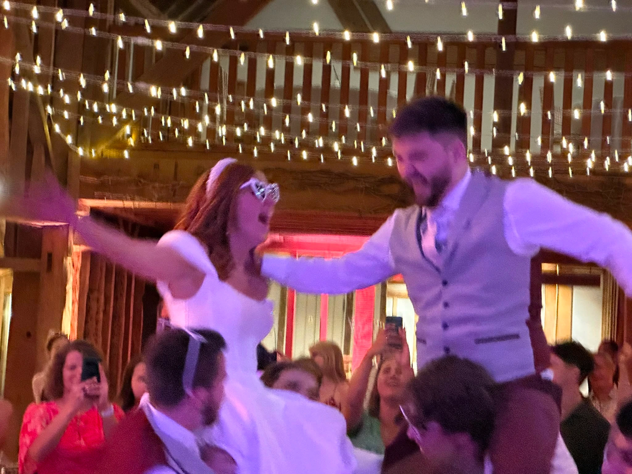 The bride and groom lifted up on shoulders under the barn fairy lights