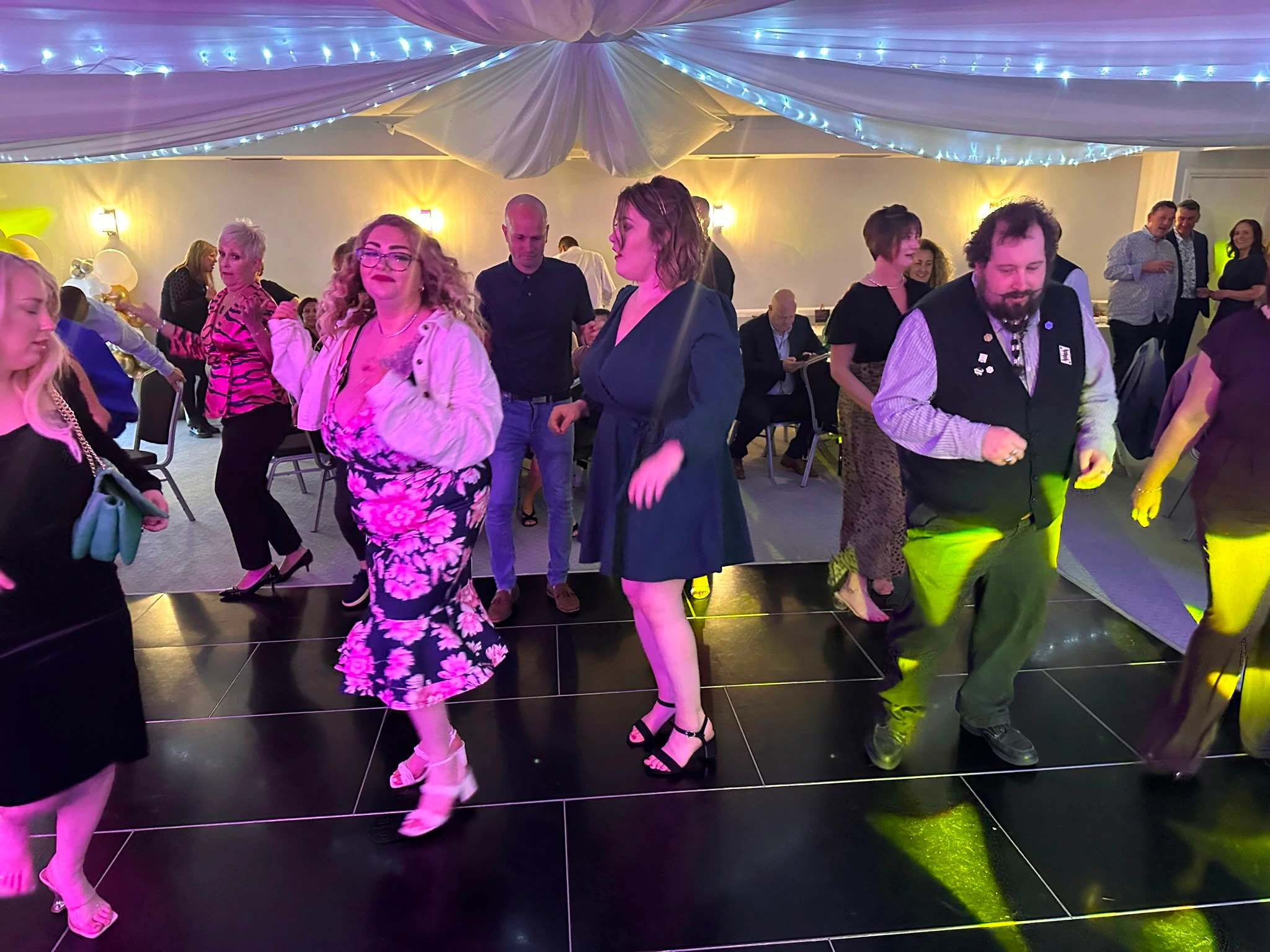 A black gloss dance floor filling up beneath draped ceilings