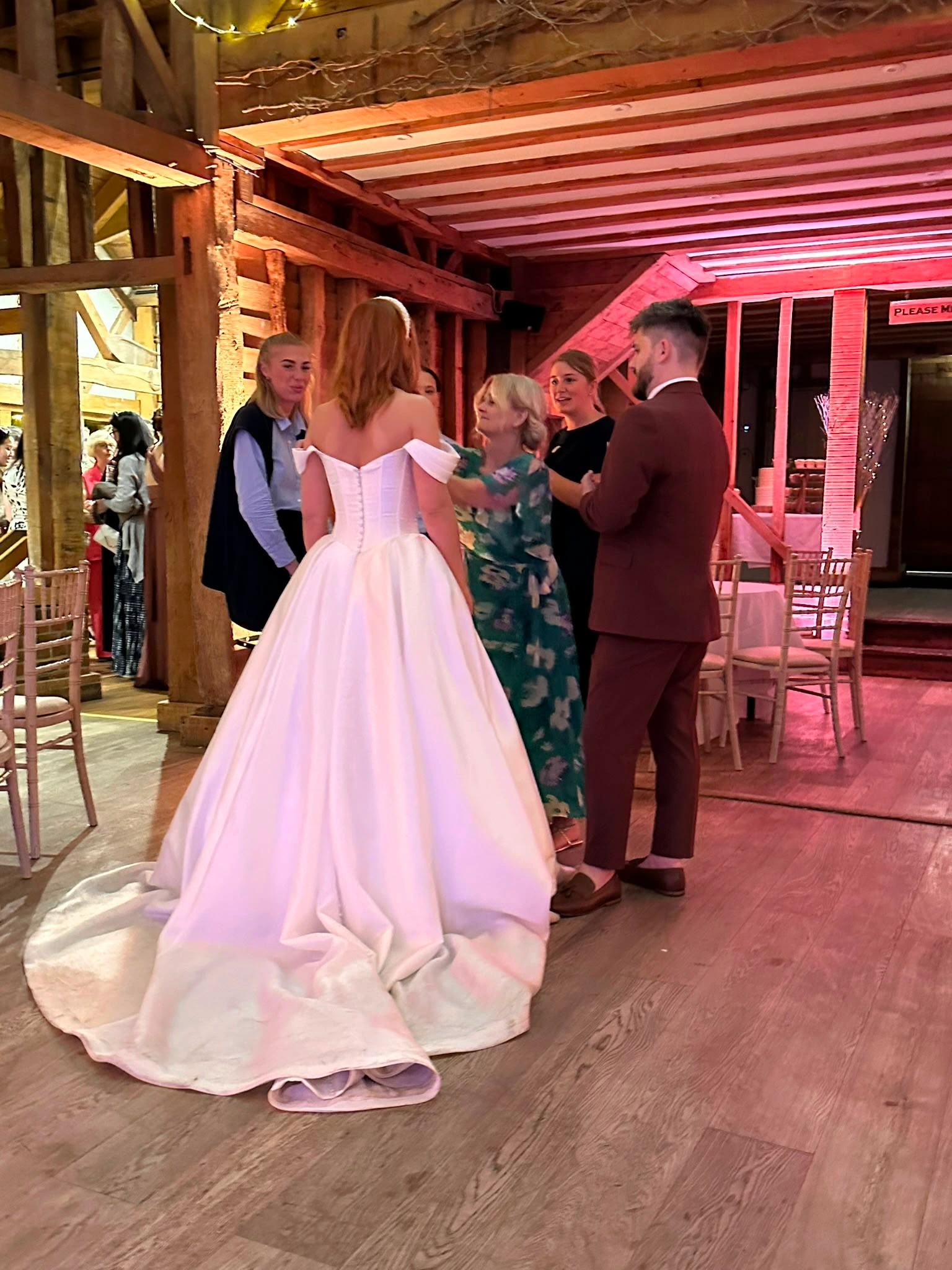 The bride in her gown among guests in a beamed barn