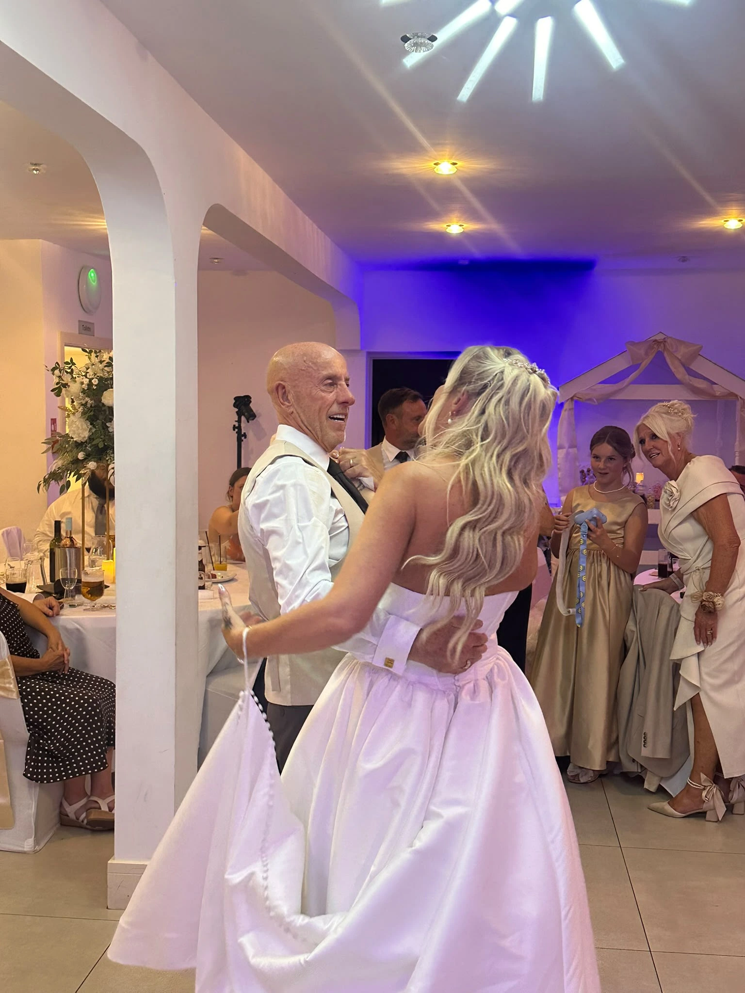 A first dance under a purple wash, guests gathered at the edge of the floor